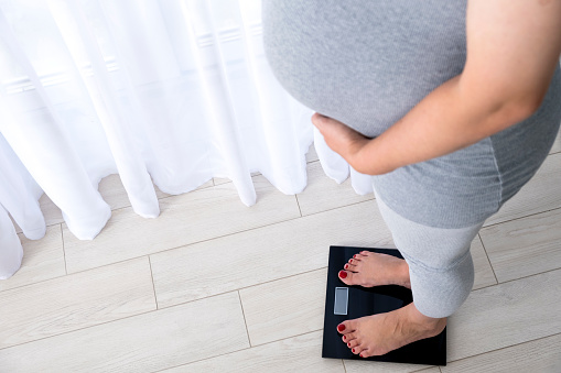 Pregnant woman on scales at home control her weight gain. Healthy pregnancy.